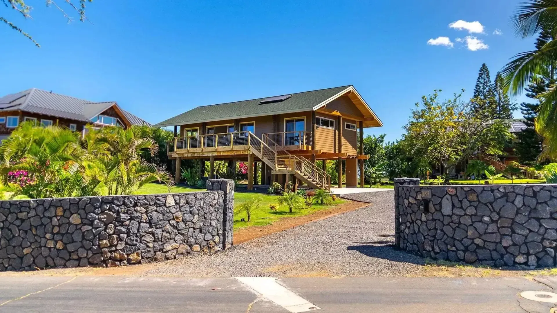 A wooden house with an elevated deck and dark stone entrance under a blue sky.