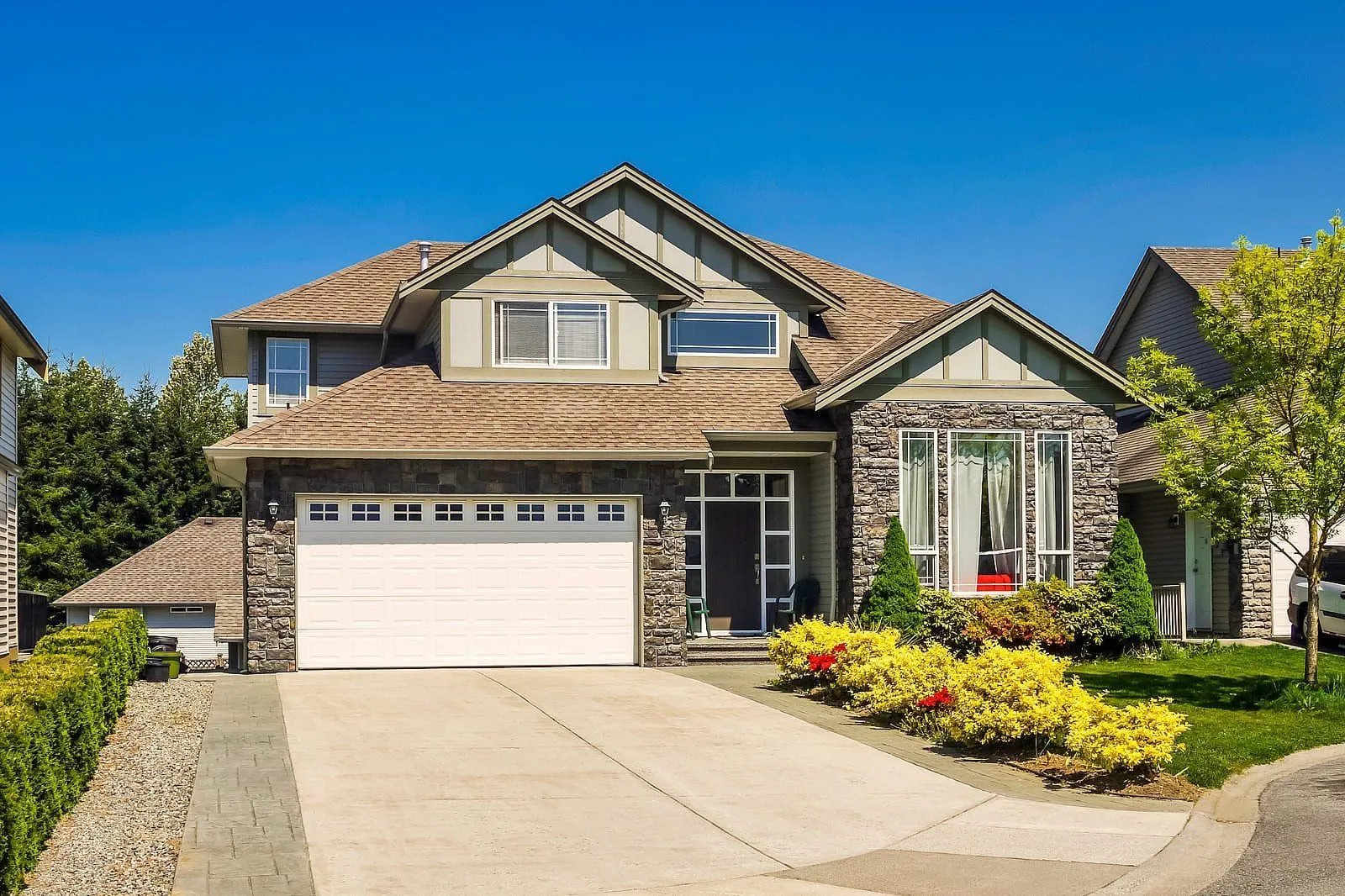 A two-story house with stone accents, an attached garage, and a landscaped yard on a sunny day.